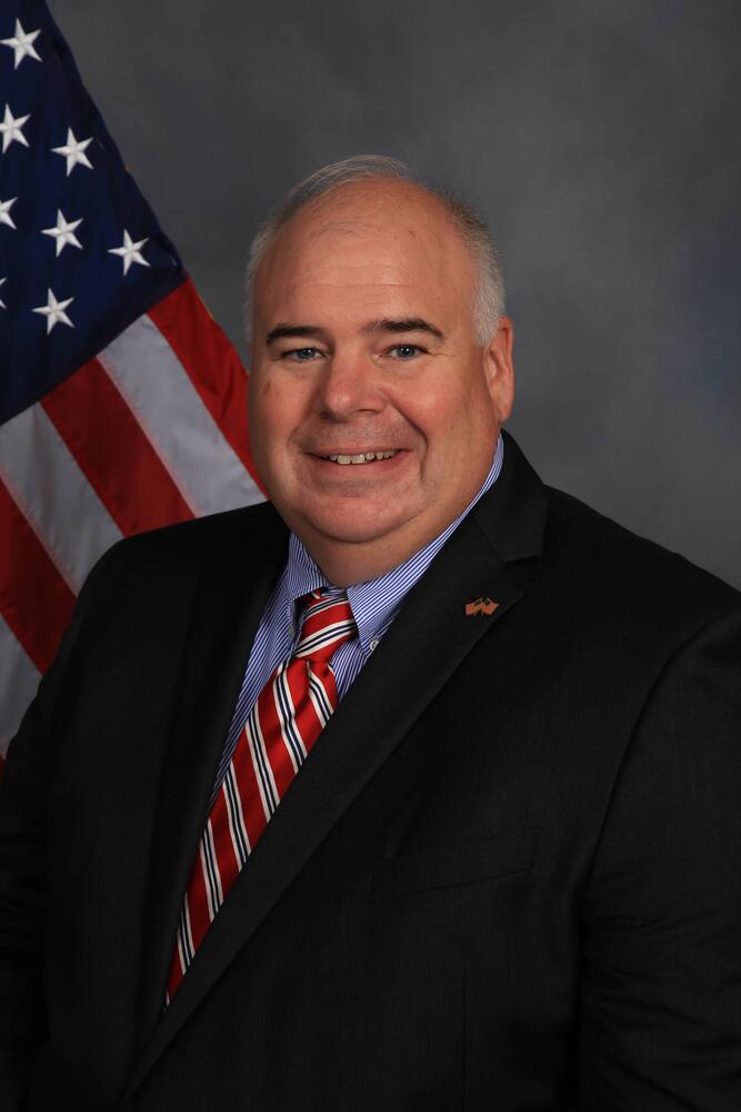 Mike Swafford in a suit in front of a flag