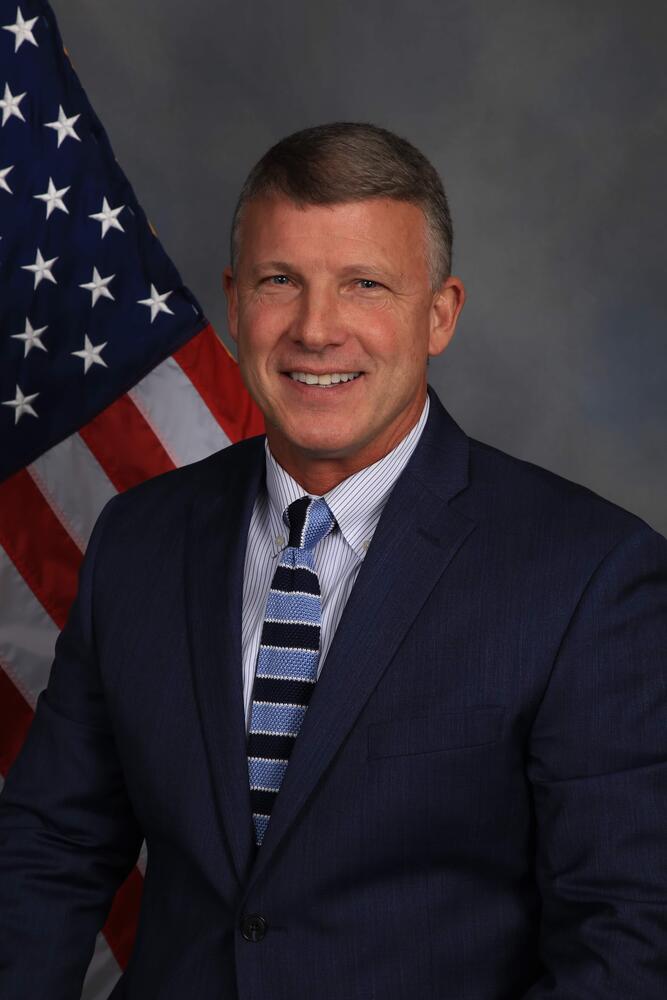 Portrait of Anthony Clark in suit in front of flag