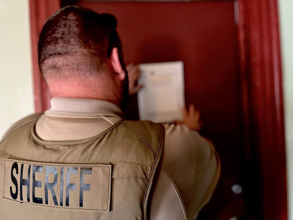 Deputy in uniform posting evictions notice on a door